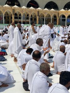 A gathering of pilgrims in white ihram garments praying at Masjid al-Haram, Mecca.