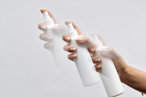 Multi-exposure shot of a hand with manicured nails holding a white spray bottle with a motion blur effect.